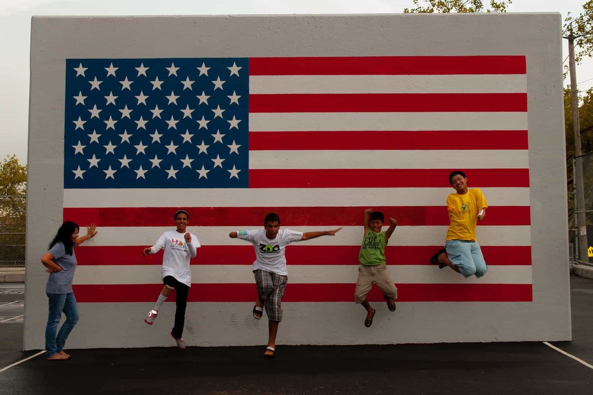 Children and a GMRF volunteer jumping and posing in front of a large American flag mural